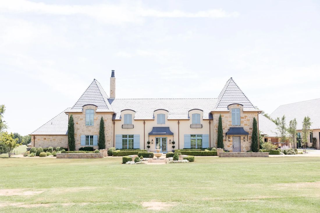 The Bower, a French-style stone estate with slate roofs, tall cypress trees, and a wide lawn